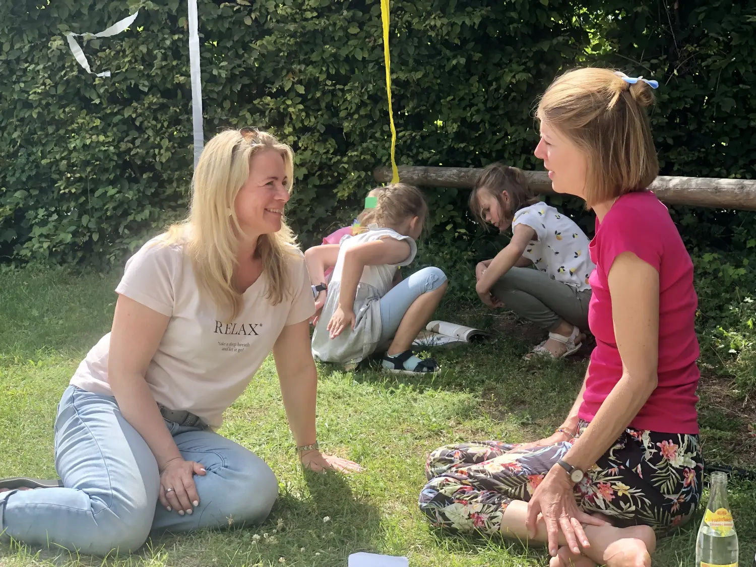 Kirsten Kau - im Gespräch mit einer Dame im Freien und Kindern, die im Hintergrund ein Buch lesen