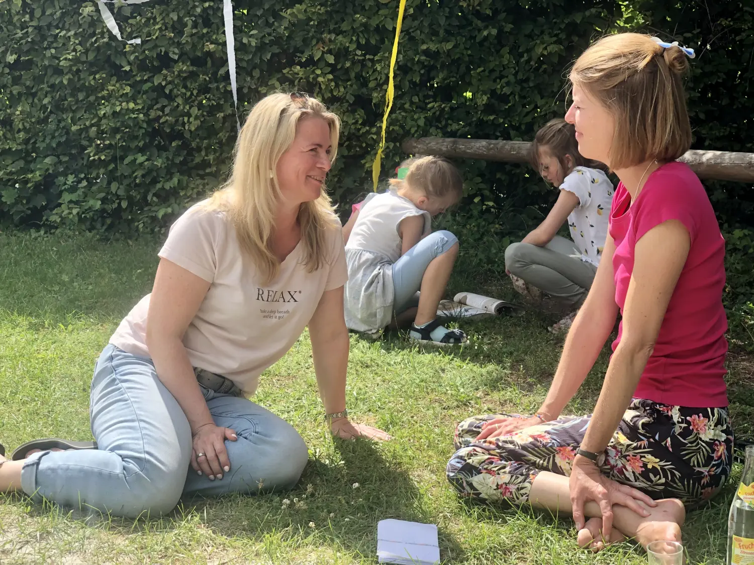 Kirsten Kau - im Gespräch mit einer Dame im Freien und Kindern, die im Hintergrund ein Buch lesen